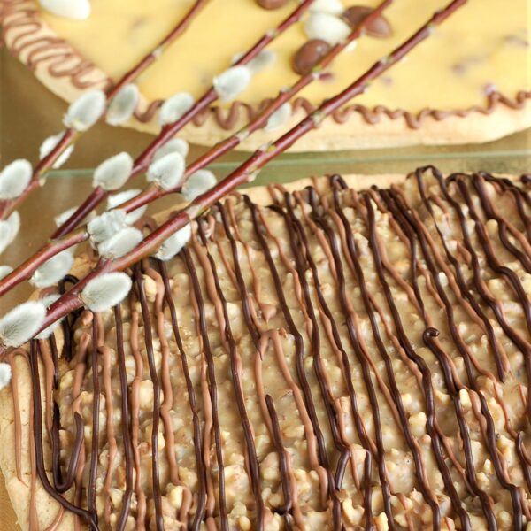 mazurek na kruchym spodzie w kształcie jajka z orzechami i pomada śmietankową, ozdobiony paskami czekolady mlecznej i gorzkiej